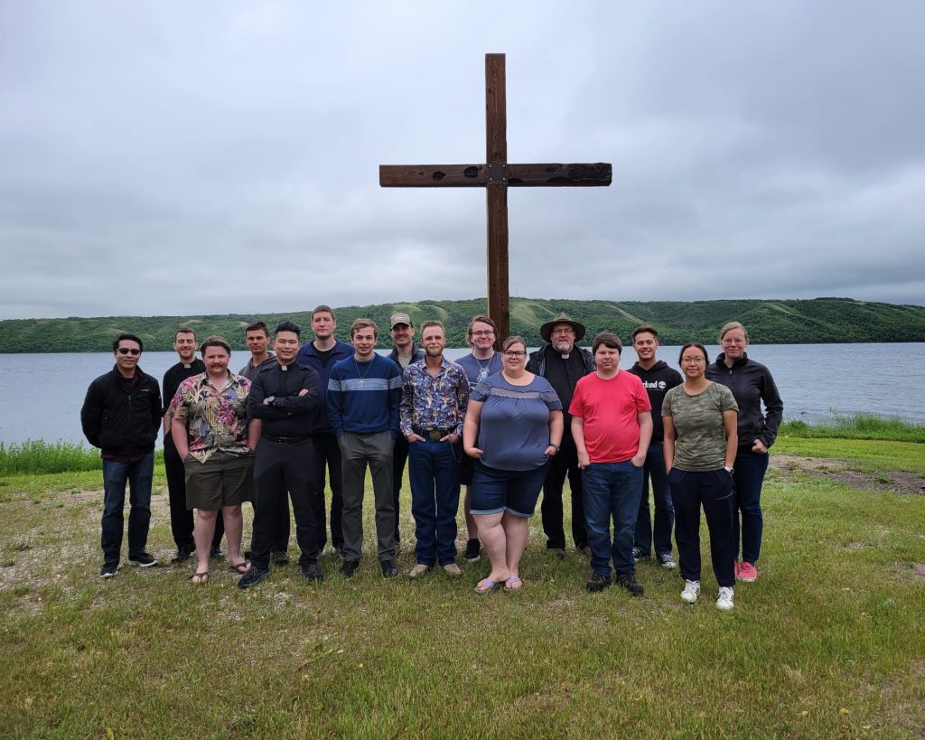 Young men and women stand in front of a large cross at Camp Lutherland.
